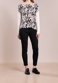 Czarny i biały top w kwiatowy wzór, z długimi białymi rękawami; zestawiony z dopasowanymi czarnymi spodniami i czarnymi błyszczącymi butami. Gładka faktura, luźny krój.