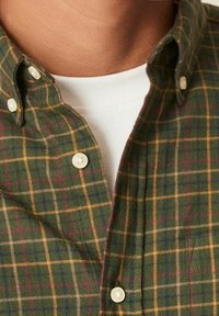 Herenflanellen overhemd met een groen ruitpatroon met gele en bordeauxrode accenten, knoopkraag en een wit T-shirt met ronde hals eronder.