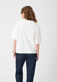 White short-sleeve shirt with a relaxed fit, paired with dark blue denim jeans. Smooth texture, minimal design, and no visible patterns or accents.