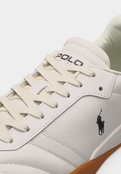 Λευκό δερμάτινο αθλητικό παπούτσι με μπεζ κορδόνια, μαύρο λογότυπο Polo στο πλάι και καφέ λαστιχένια σόλα ορατή στην άκρη.