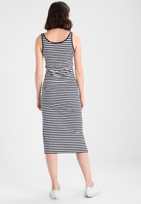 Wzorzysta sukienka midi w kolorze granatowym i białym, charakteryzująca się dopasowanym krojem, bez rękawów oraz gładkim materiałem. Noszona z białymi sneakersami.