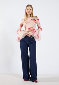 Haut en chiffon floral avec des manches évasées en rose clair, avec un décolleté carré. Assorti à un jean en denim bleu foncé à jambes larges.