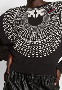 Černá mikina s kulatým bílým grafickým vzorem obsahujícím text a siluety, žebrovanými manžetami a zakončením na gumu.