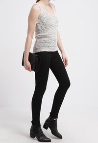 Top in cotone bianco a maglia, jeans skinny neri, stivaletti neri alla caviglia con borchie argentate e una borsa a tracolla nera. Design semplice, senza motivi.