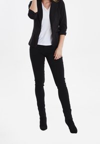 Svart blazer med rullade ärmar över en vit V-ringad t-shirt, kombinerad med svarta skinny jeans och knähöga svarta stövlar.