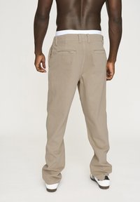 Beige bomuldsbukser med lige ben, udstyret med sidelommer, to baglommer og et hvidt taljebånd.