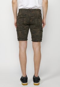 Khaki Cargo-Shorts mit strukturiertem Muster, elastischem Bund, mehreren Taschen und geradem Schnitt, kombiniert mit schwarzen Sneakers.
