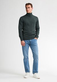Pulover negru închis cu guler înalt, în croială ajustată, realizat dintr-un material moale, asortat cu blugi albastru deschis și adidași albi.