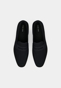 Μαύροι loafers με επενδυμένη επάνω πλευρά, διακριτές λεπτομέρειες ραφής και πλεκτή ζώνη στη κορυφή. Λείος υφή, μινιμαλιστικός σχεδιασμός.