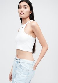 Top corto blanco de canalé con un cuello alto y corte lateral, con el logo "OFF" en negro, combinado con jeans de mezclilla azul claro.