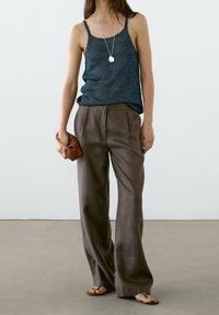Débardeur bleu foncé texturé associé à un pantalon large en lin marron taille haute. Accessoirisé d'une petite pochette tissée et d'un collier pendentif en argent.