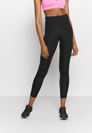 Zwarte hoge taille leggings van rekbaar materiaal, met een gladde textuur en een slim fit ontwerp, gecombineerd met zwarte sportschoenen en een roze top.