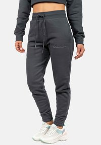 Dunkelgraue Jogginghose mit einem Kordelzugbund, gerippten Knöcheln und dezentem Logo-Detail. Der Stoff wirkt weich mit einer glatten Textur.