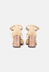 Žluté vysoké boty na podpatku s uzavřenou špičkou, kotníkovým páskem a blokovým podpatkem s kovovým povrchem. Hladký kožený vzhled.