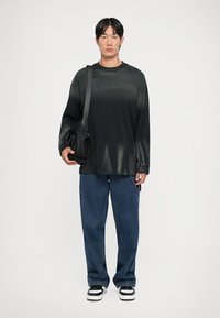 Svart langermet skjorte med en subtil ombre-effekt, kombinert med løse blå denimjeans og svart-hvite joggesko. Svart crossbody-veske.