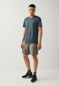 T-shirt de sport gris foncé, short cargo beige avec poches latérales, baskets noires avec accents blancs, chaussettes grises. Style simple et fonctionnel.