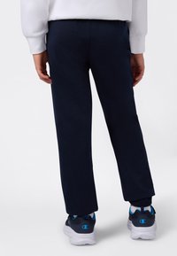 Navyblå joggebukser med elastisk liv, rette ben og ribbede mansjetter. Kombinert med svarte joggesko med blå detaljer.