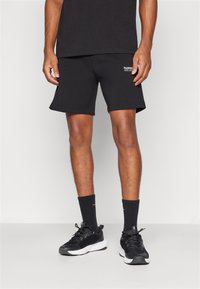 Calções atléticos pretos com um ajuste confortável, feitos de um tecido suave. Combinados com meias pretas e sapatilhas pretas desportivas com solas brancas.