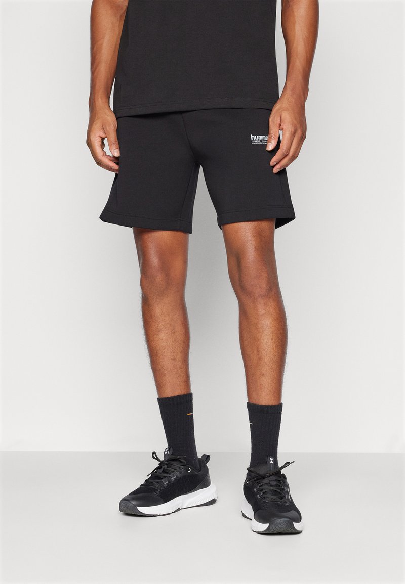 Calções atléticos pretos com um ajuste confortável, feitos de um tecido suave. Combinados com meias pretas e sapatilhas pretas desportivas com solas brancas.