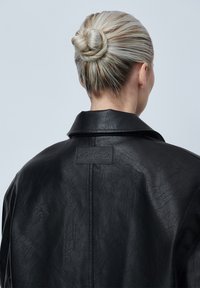 Veste en cuir noir oversize avec une finition texturée et col rabattable. Dotée d'une patch de marque "LeGer Studio" dans le dos.