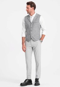Chaleco a cuadros gris con solapa muesca, botones, camisa blanca, pantalones grises y zapatos de cordones negros. Diseño sencillo y a medida.
