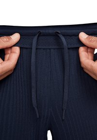 Pantaloni felpati a coste blu navy con cintura regolabile, caratterizzati da un tessuto testurizzato e un bordo superiore a maglia piatta. Due mani afferrano la zona della vita.