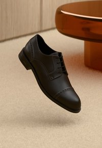 Zwarte leren Oxford schoen met een gladde textuur, een ronde neus en decoratieve brogue details aan de voorkant. Veters in het midden.