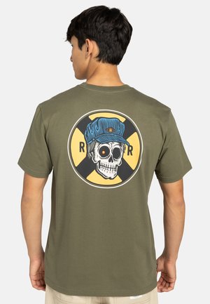 Olivgrön bomull t-shirt med en stor grafik av ett skelett som bär en blå keps, placerad mot en cirkulär gul och svart design.
