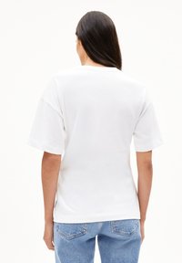Weißes Baumwoll-T-Shirt, kurze Ärmel, lockere Passform, runder Ausschnitt, schlichte Rückseite, seitliche Schlitzungen am Saum, kombiniert mit blauen Jeans.