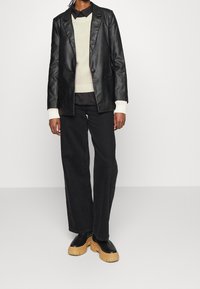 Svart läderblazer med enstaka knappstängning, tillsammans med en krämfärgad stickad tröja. Svarta vida jeans och svarta platåskor fulländar looken.