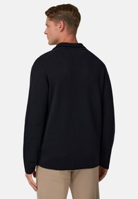 Tumesinise jumpser, millel on mugav lõige, kaelusega ja pikad varrukad, valmistatud pehmest kangast, millel on sile tekstuur.