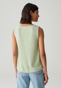 Top senza maniche verde chiaro realizzato in tessuto testurizzato, con scollatura rotonda e vestibilità rilassata, abbinato a jeans in denim blu chiaro.