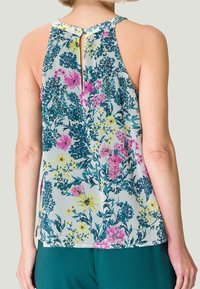 Blouse sans manches en tissu léger, présentant un dos en forme de trou de serrure, avec des fleurs roses et jaunes vives sur fond bleu clair, et une coupe décontractée.