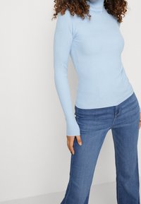 Lichtblauwe geribbelde coltrui met lange mouwen, aansluitend ontwerp, gecombineerd met hoge taille blauwe flared jeans. Gladde stoftextuur.