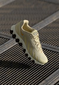Gaišdzeltenas sporta apavi ar gludu tekstūru, izliekta silueta un izteikts oranžs Nike swoosh. Aprīkoti ar masīvu zoli ar tumšiem akcentiem.