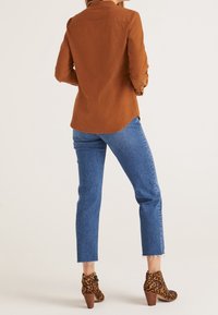 Camicia marrone a maniche lunghe con orlo curvo, abbinata a jeans blu a vita alta e stivaletti con tacco a stampa leopardata con finitura testurizzata.