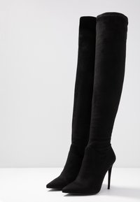 Stivali alti neri sopra il ginocchio realizzati in morbido suede, con punta affusolata, tacco a stiletto alto e un design elegante e aderente.