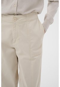 Beige bomullbyxor med rak passform, med knappknäppning fram, sidofickor och synliga sömdetaljer.