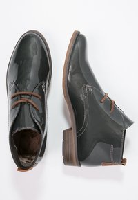 Bottes de cheville en cuir noir brillant avec des lacets marron, des coutures contrastées, un talon marron et une doublure intérieure douce. Design à bout rond.