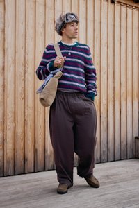 Multicolored sweater with horizontal stripes in pink, blue, and green; loose brown pants; fur hat; beige bag with a patterned cloth.