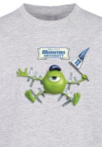 Grå T-shirt med en grøn tegneseriefigur med et stort øje, der holder en blå fane, omgivet af strimler af tape.