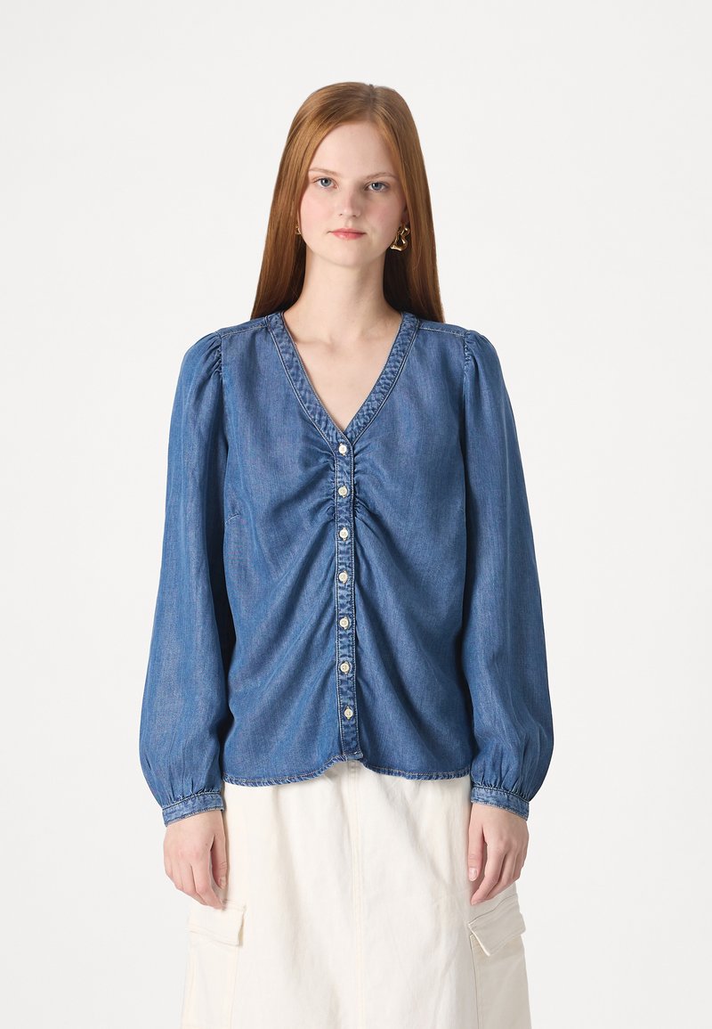 Denim särk V-kaelusega, eest nööbistamisega, pikkade puffvarrukatega ja kogumise detailidega taljes. Pehme sinine värv koos õmblusaksentidega.