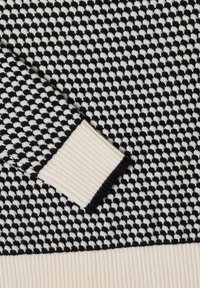 Sweter w czarno-białe wzory z teksturowaną powierzchnią. Białe, prążkowane mankiety i dół kontrastują z geometrycznym wzorem.