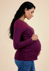 Top de maternitate în violet cu dungi orizontale albastre, mâneci lungi, decolteu rotund, asortat cu blugi blue. Țesătură netedă, formă ajustată.