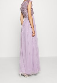 Dlouhé, levandulové šaty s korálkovou korzetou a volánovými rukávy. Padající, průhledná sukně s rozptýlenými ozdobami a hladkou strukturou.