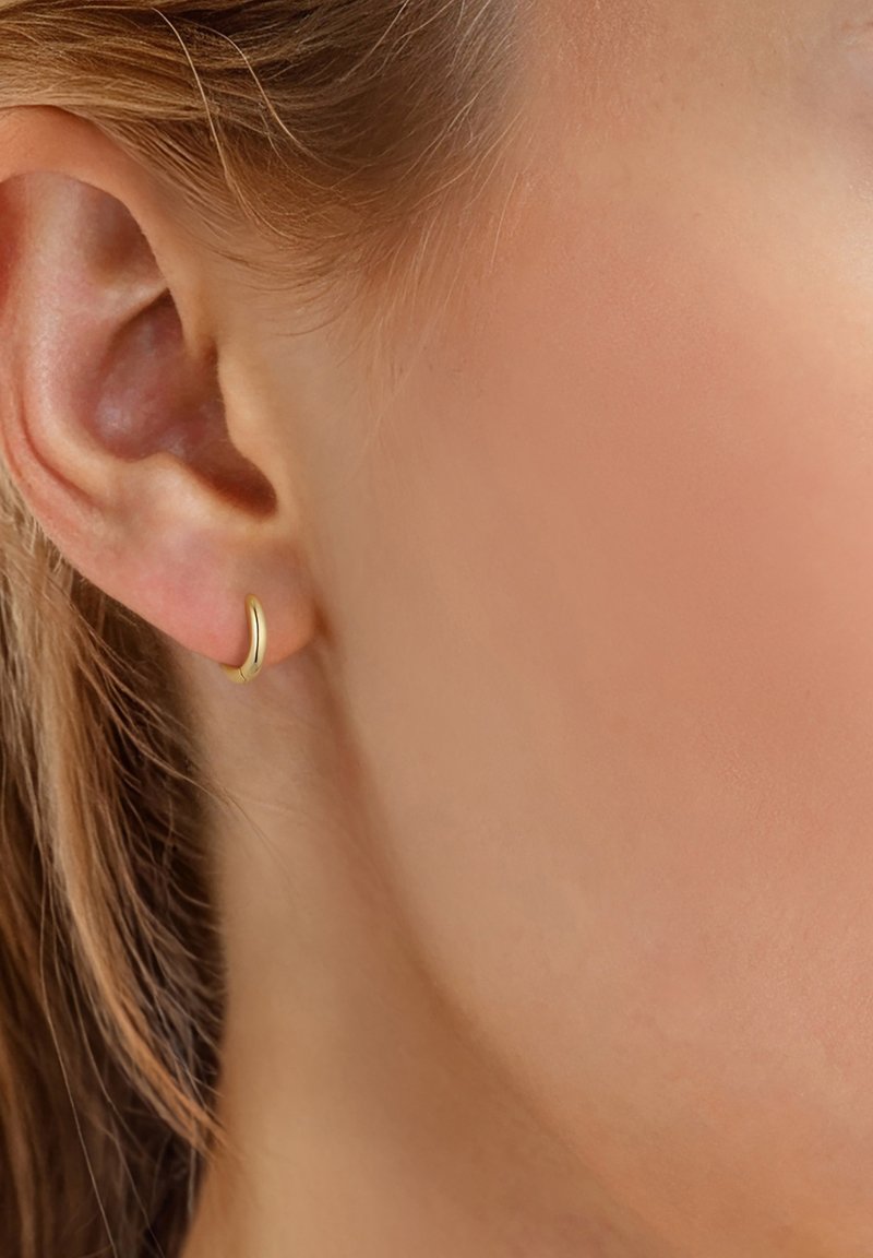 Zlatna omča s naušnicom u zakrivljenom, minimalističkom dizajnu. Glatka, sjajna površina s elegantnim profilom. Nosena na režnju uha.