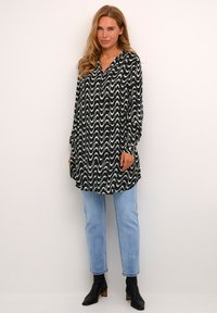 Blouse à motifs noir et blanc avec un col en V, des manches longues et une coupe ample, assortie à un jean bleu clair et des bottines.