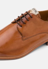 Scarpa da dress in pelle marrone con finitura liscia, punta tonda, presenta cuciture in tono, sei fori per i lacci e un tacco basso.