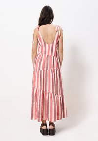 Maxi-Kleid in rot-weiß gestreift mit tiefem Rückenausschnitt, gestuftem Design, Bindeträgern und kombiniert mit dunklen Plateausandalen.