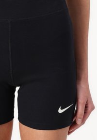 Shorts de sport noirs en matière extensible. Dotés d'un logo Nike blanc en bas à droite et de coutures plates pour le confort.
